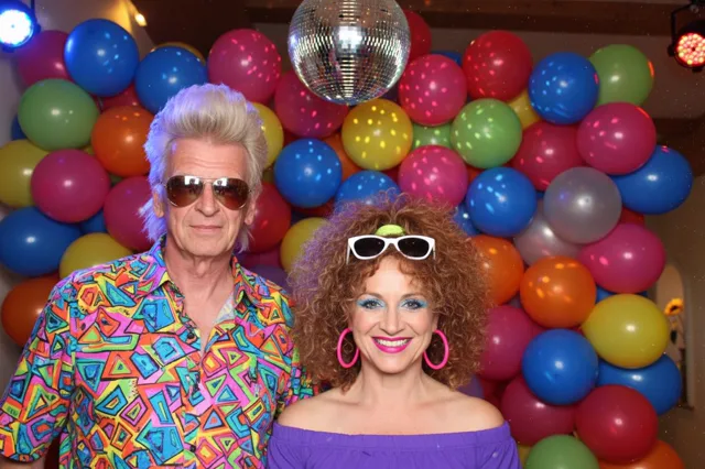 Paar im 80er-Look vor Ballonwand mit Discokugel – Fotobox-Foto