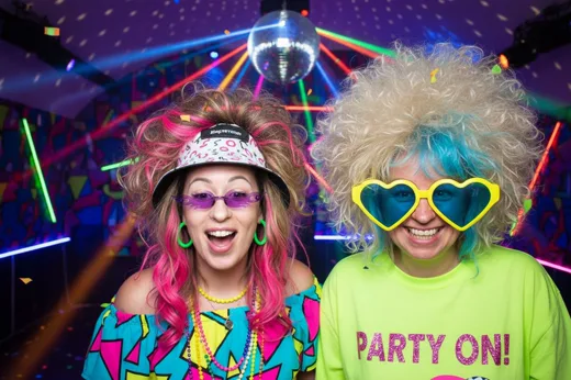 Zwei Freundinnen mit Perücken und Herzbrillen auf einer Neon-Party